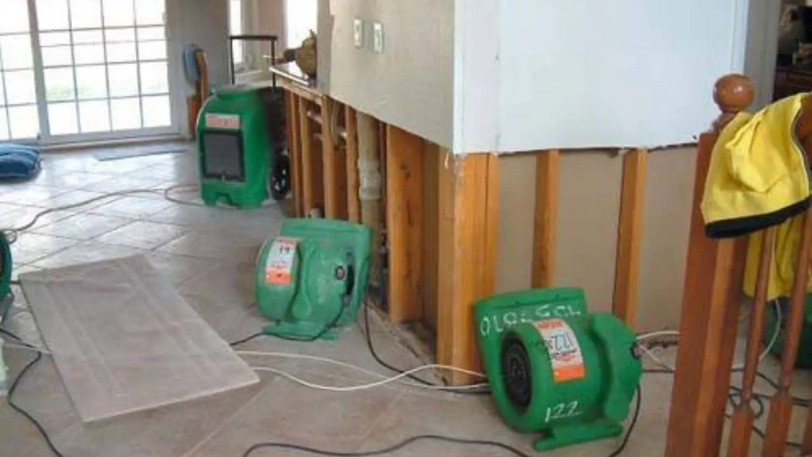 Green air movers drying a room after wet drywall was cut out of the lower wall